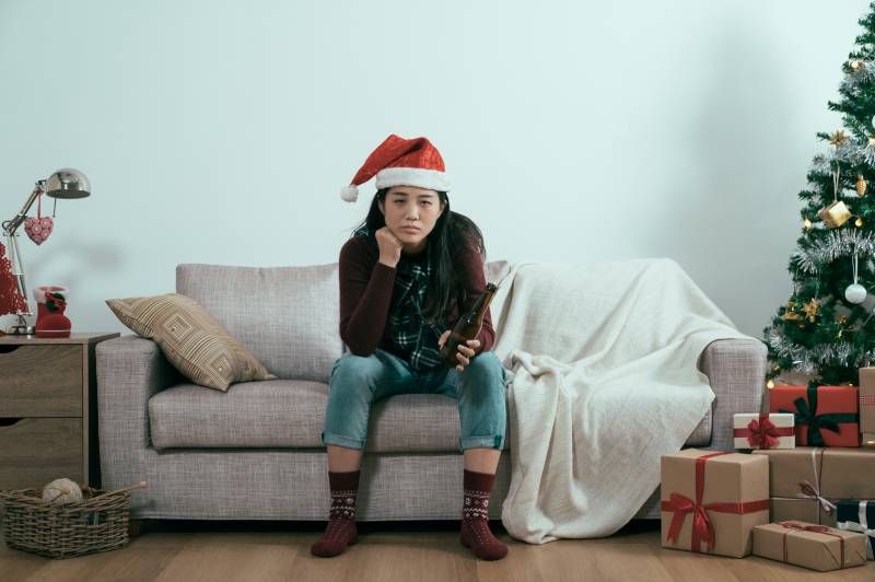 An Asian person with long hair and Santa hat sitting in a living room decorated for the holidays.  This could represent the unhappiness one feels and wanting a fulfilling life in Ontario, CA.  Learn more about how a therapist in Ontario can offer support for your relationship. Search for “lack of fulfillment in life in Ontario, ca” today.