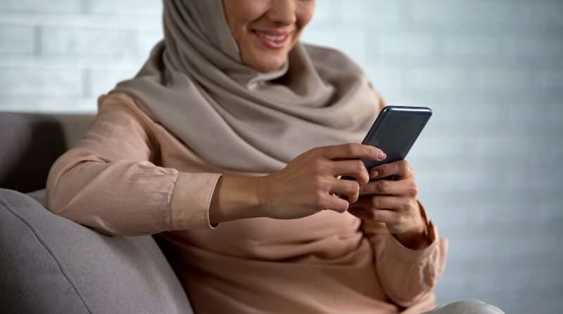 A hijabi smiling while using their phone.  This could represent a life fulfillment in Ontario, CA. Learn more about how a therapist in Ontario can help you feel fulfilled in life.   