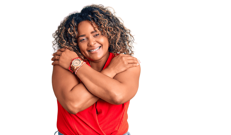 A black woman smiles softly while giving herself a hug. This could symbolize overcoming signs of an unfulfilled life in Toronto, CA. Learn more about finding self fulfillment in Ontario, CA by contacting an Ontario therapist today.