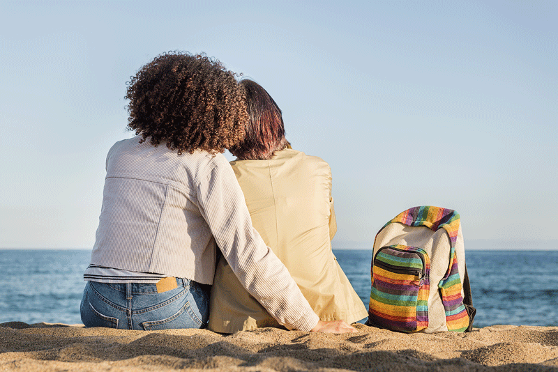 A lesbian couple sit together while looking out over the ocean. Learn how a therapist in Ontario can offer support for your relationship. Search for support in creating a more fulfilling relationship in Ontario, CA today.