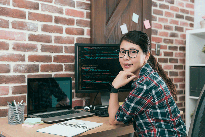 A person sitting at a computer desk while smiling at the camera. This could represent finding creative solutions at work. Finding self fulfillment in Toronto, CA at work is possible when working with a self fulfillment therapist in Ontario, CA.